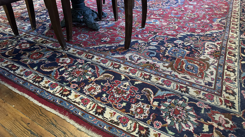 A red and blue Persian rug with floral detailing on the floor under a table and chairs