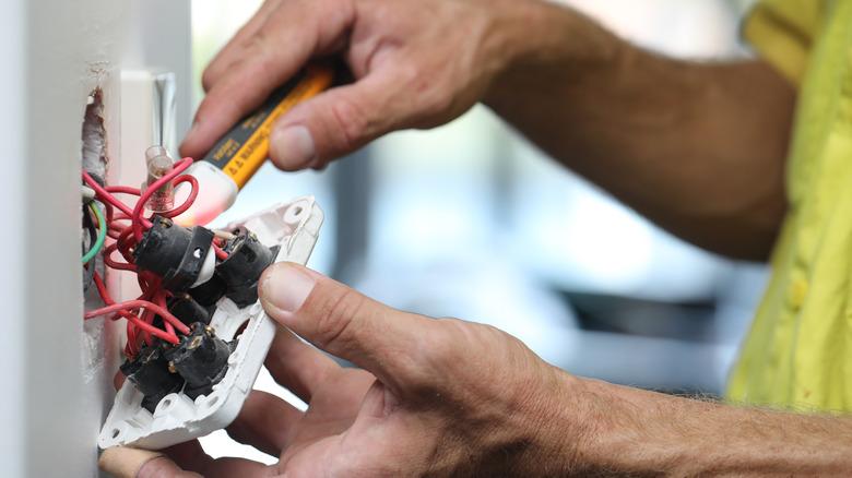A close up of an electrician working on a light switch