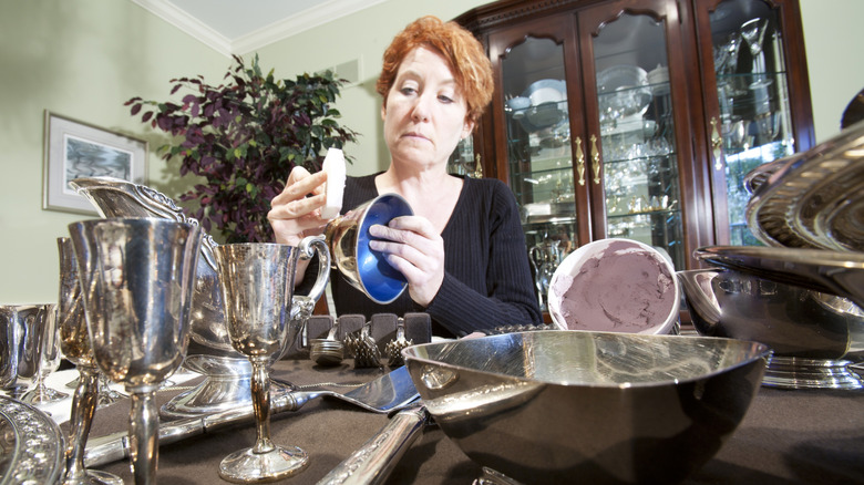 A Person using silver cream to polish a range of assorted silverware