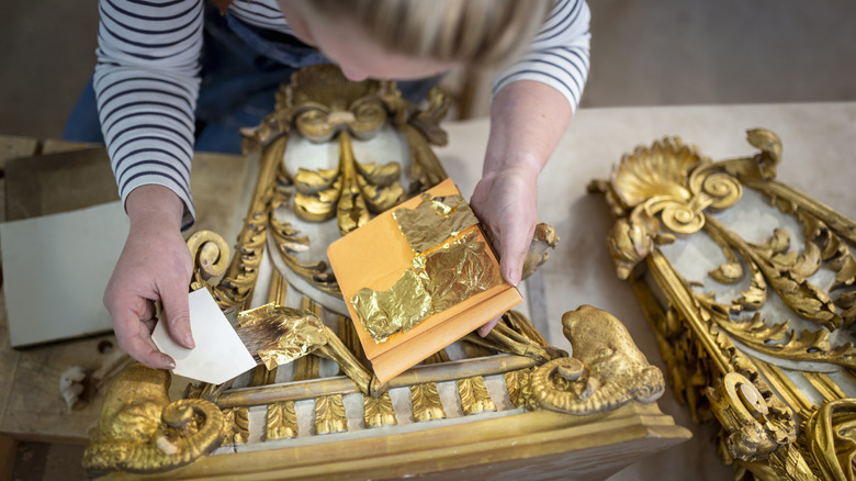 An overhead shot shows a woman applying gold leaf to gilded decorative elements