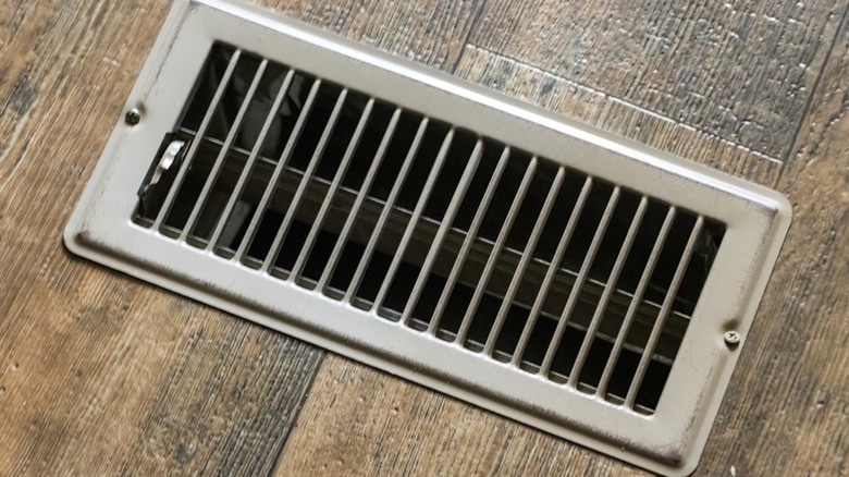A wooden floor with a gray floor vent
