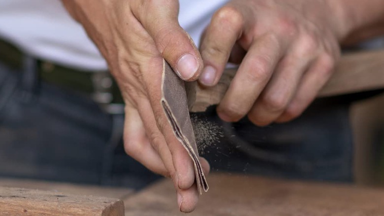 A person uses a sheet of sandpaper on a chair leg