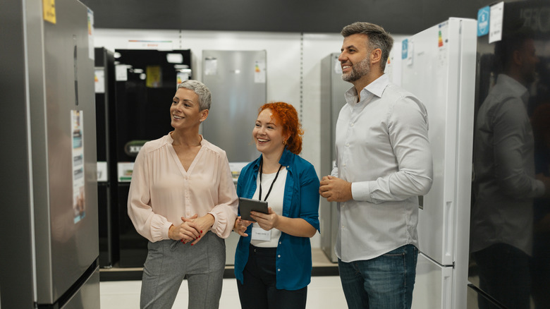 Three people examine a refrigerator in an appliance store fridge aisle