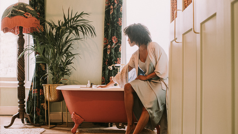Woman sitting on side of bathtub in bathroom with floral decor