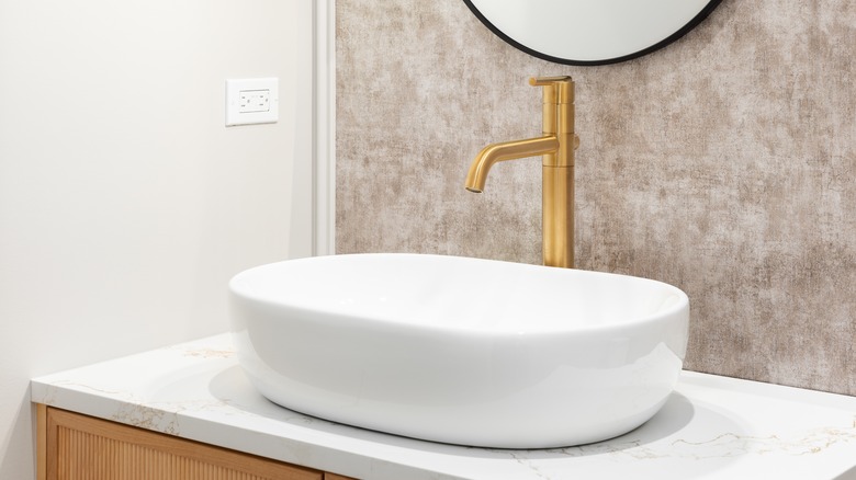 Bathroom with a white sink, gold faucet, and textured backdrop