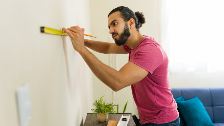 Man using tape measure on wall inside apartment