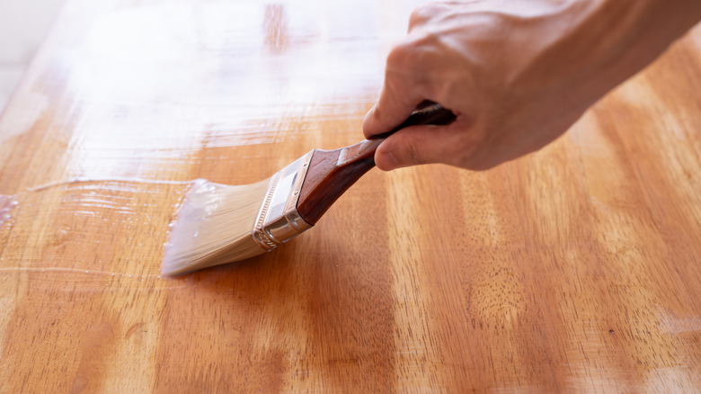 Hand applying a clear polish to wood with a brush