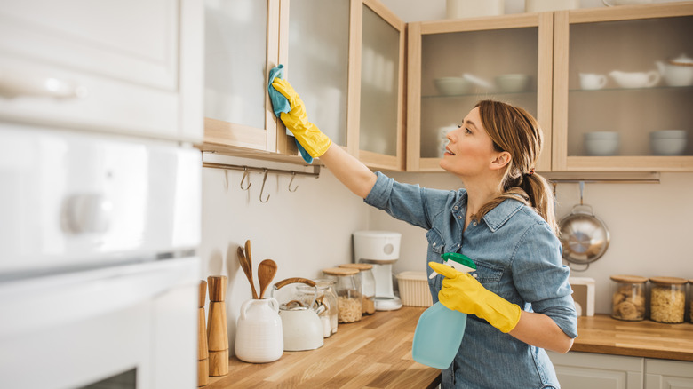 Woman cleaning kitchen cabinets with cloth