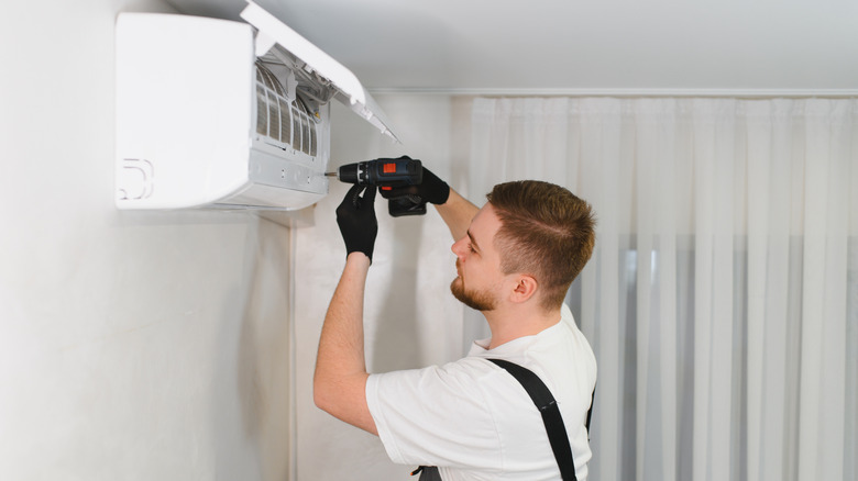 Repair tech using a drill on an indoor AC unit