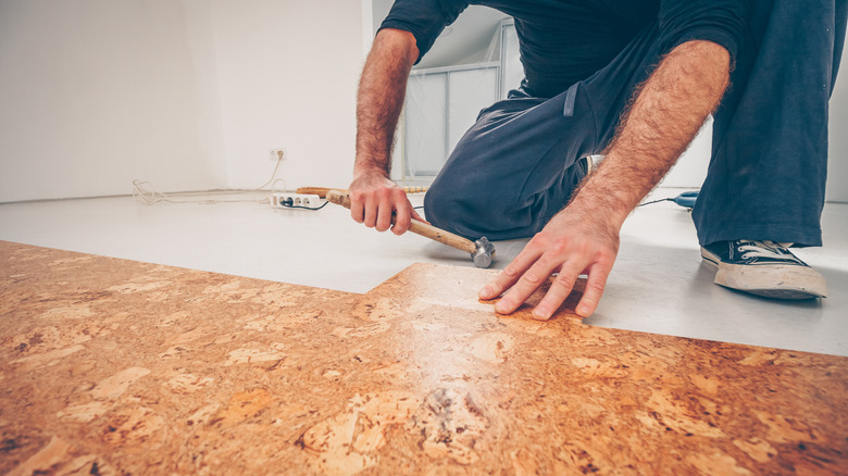 A carpenter carefully installs a series of cork flooring planks using a hammer, showcasing the natural texture and warm tone of cork floors.