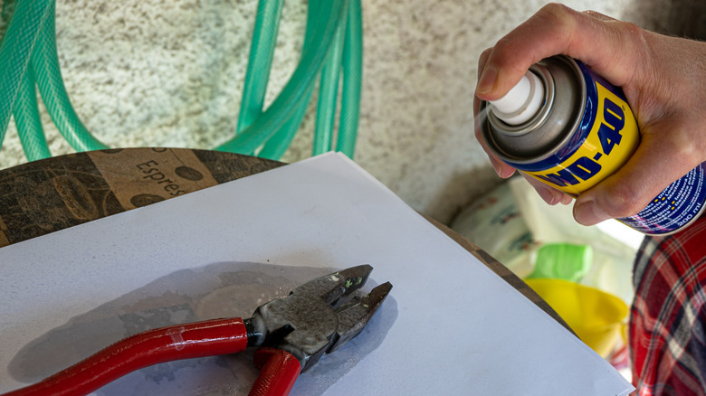 A canister of WD-40 penetrating oil being sprayed on a pair of pliers.