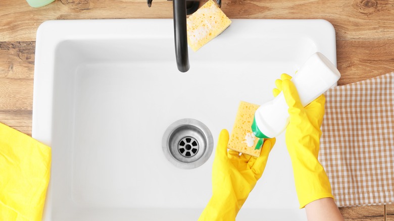 Gloved hand adds soap sponge sink