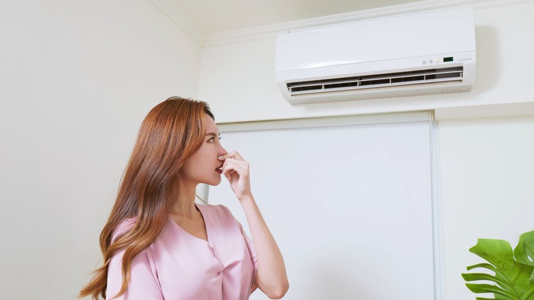 A woman covering her nose because of a bad smell coming from a heater