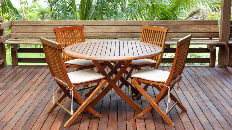Golden-hued teak dining table and four chairs with cushions on a tropical deck
