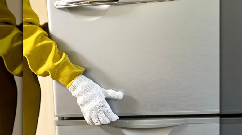 Gloved hands moving refrigerator