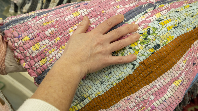 Person's hand runs over a knotted rug featuring pink, green, yellow, brown, and other colors in the design