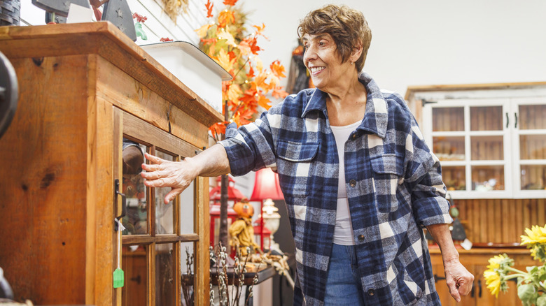 A woman smiling while shopping for vintage wood furniture in a secondhand store