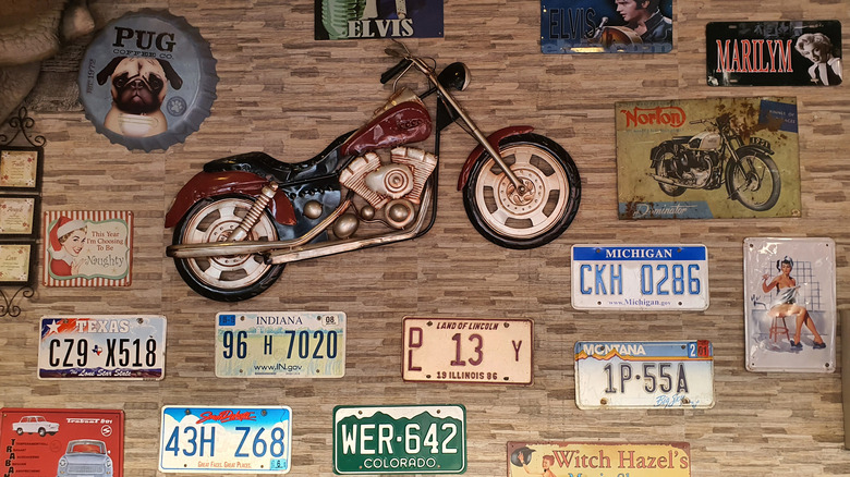 Collage wall with vintage licenses plates, motorcycle decal, and posters