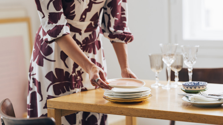 A woman in a dress setting a table with fine dishware.