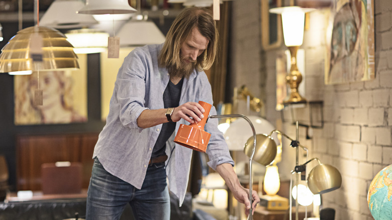 Man adjusting gooseneck lamp in lighting section of a shop