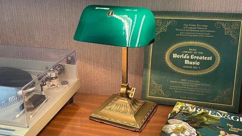 Emeralite banker's lamp with ornate brass base on wooden desk next to record player