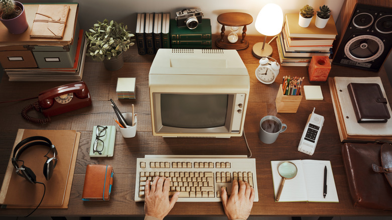 Hands typing on a keyboard surrounded by a plethora of vintage items.