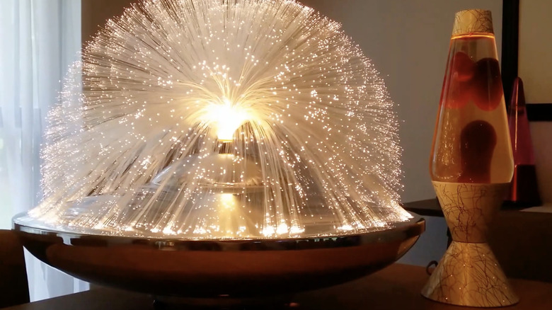 A glowing fiber optic lamp displayed on a bedside table along with a lava lamp.