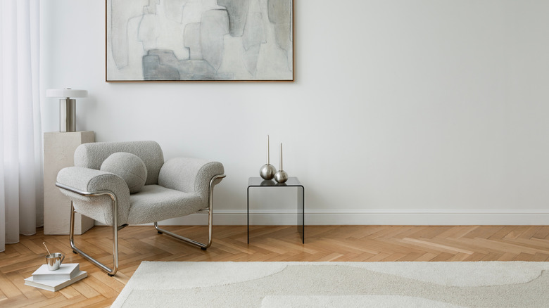 A reading nook is created in the corner with a gray and silver armchair, sleek black stand, and a neutral-colored lamp behind the chair.