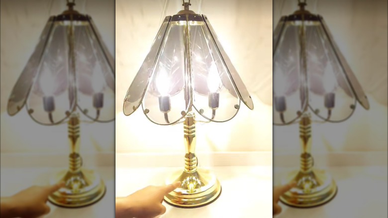 A light-skinned hand turns on a vintage '80s touch lamp.