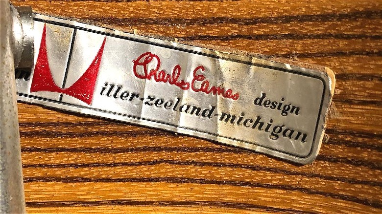 A metal Charles Eames Herman Miller logo stamped on the bottom of a furniture piece.