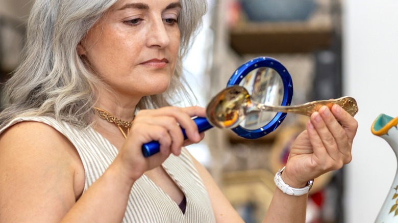 A person inspects the back of a spoon with a magnifying glass