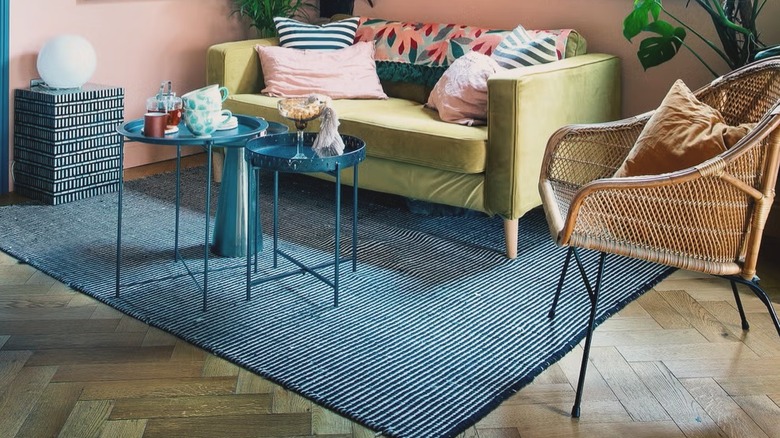 Living room with peach walls, rattan chairs, and green sofa on a blue rug