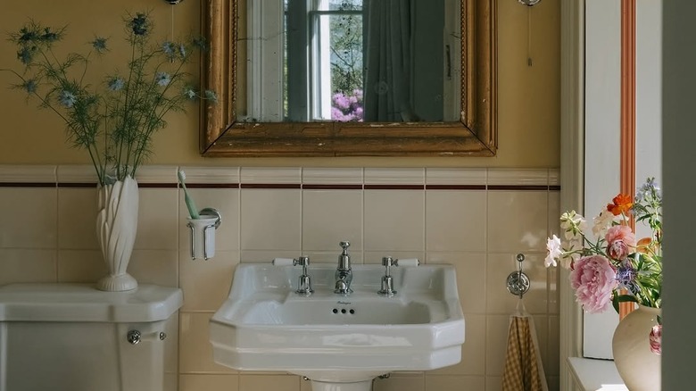 A bathroom with a cream tile backsplash and red tile border