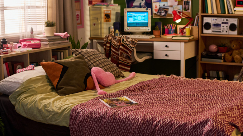A teen bedroom with a patterned blanket on the bed and an old PC and a boom box.