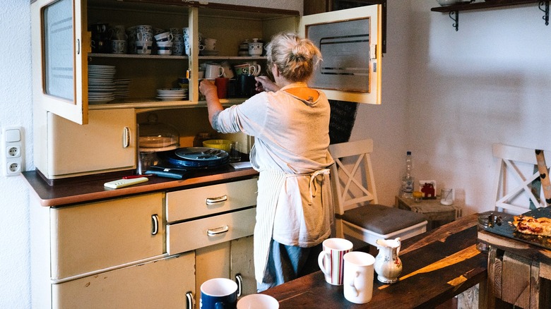Person reaching into an open cabinet of what could pass for a '50s kitchen