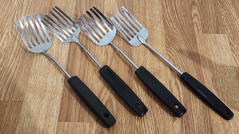 Four stainless steel Foley forks sit on a wooden countertop.