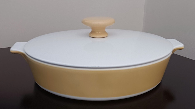 A dish from CorningWare's butterscotch line featuring a yellow dish, a white lid, and a yellow knob in the center of the lid