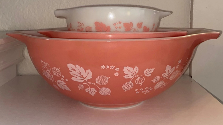 A stack of three Cinderella Gooseberry Pyrex bowls sit on a shelf in a cream-colored kitchen cabinet.
