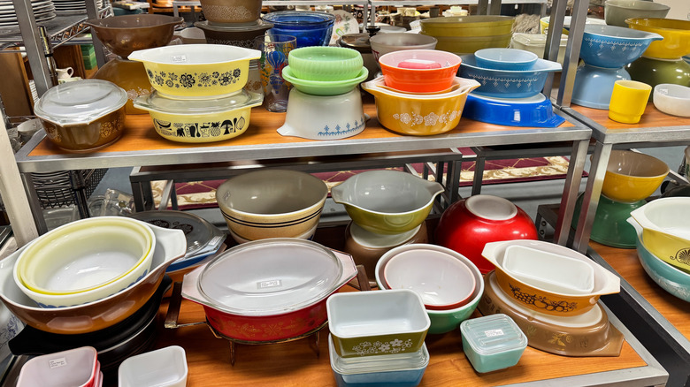 An assortment of vintage Pyrex bowls and cooking dishes on the shelves of a thrift store.