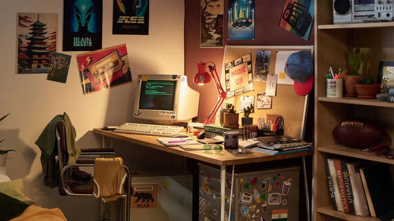 A 1980s style corner of a bedroom with a desk, bookshelf, and computer.