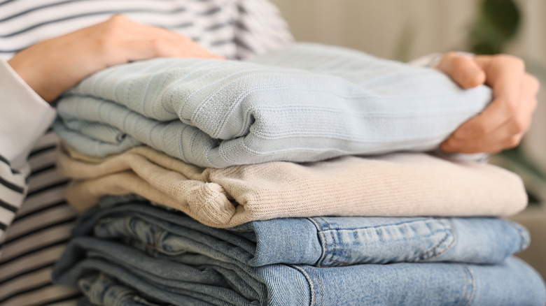 A woman with stack of stylish clothes at home