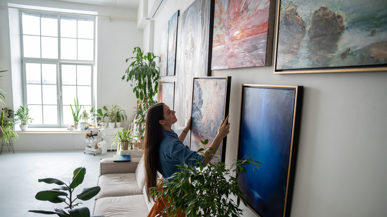 a woman hanging paintings on a wall