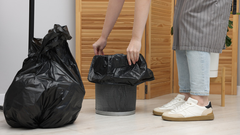 Woman putting plastic bag onto trash bin indoors
