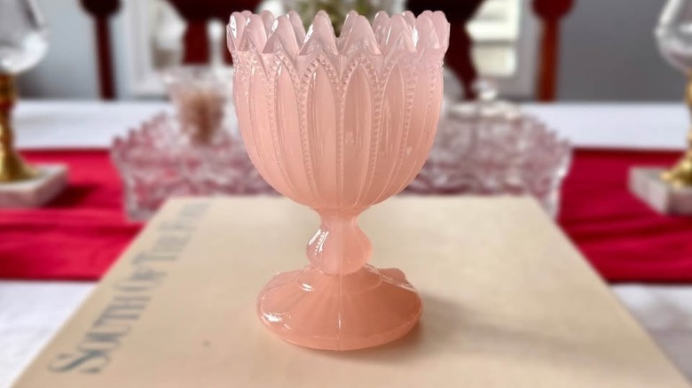 Pink opaline glass goblet set on top of a hardback book on a table