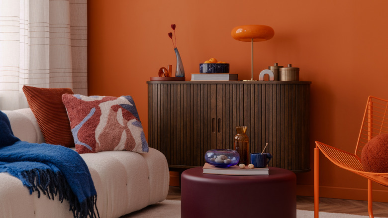 Living room with round console table, curvy sofa, and circular ottoman, orange paint on the walls