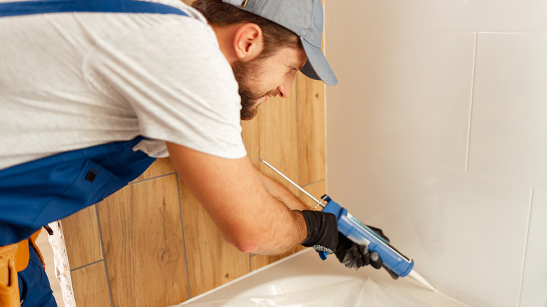 A person applies caulk between a bathtub and the wall while completing a bathroom upgrade