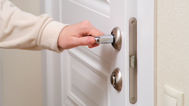 A woman in a white sweatshirt opening a door with a silver handle.