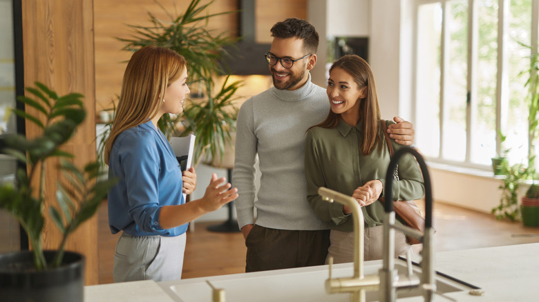 An assistant helps a young couple pick out a design in a kitchen showroom.
