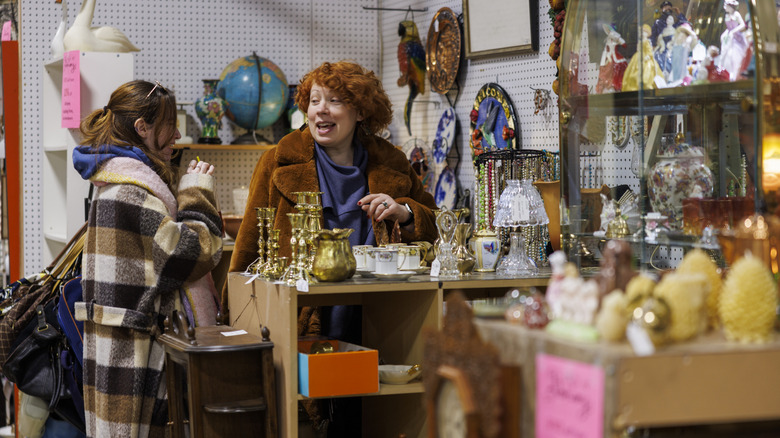 Two woman chat while shopping at a thrift store full of vintage home decor.
