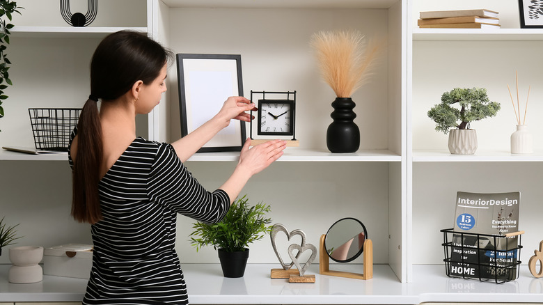 A woman placing a clock on a shelf